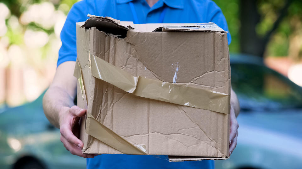 Male courier showing damaged box, cheap parcel delivery, poor shipment quality.