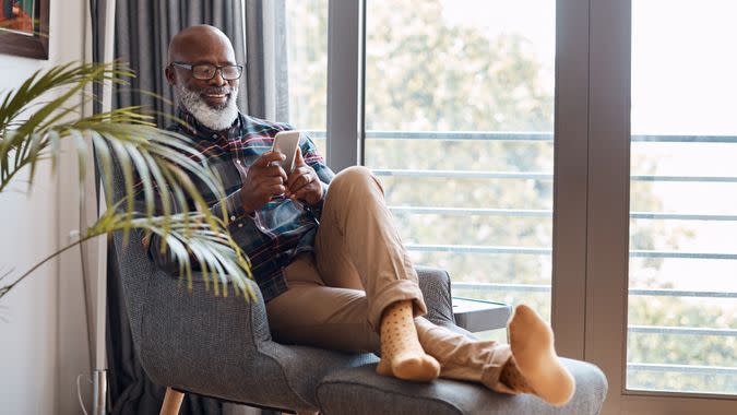 Shot of a mature man using a cellphone while relaxing on a sofa at home.