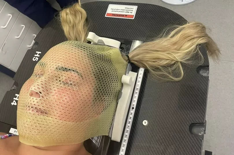 A girl undergoing a brain scan with a mask over her face as she lies on a table
