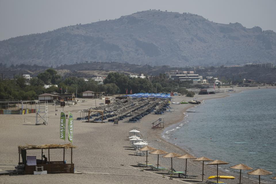 Abandoned sunbeds and umbrellas stand at the beach as a burnt hill is seen in the background after a wildfire, near Gennadi village, on the Aegean Sea island of Rhodes, southeastern Greece, on Thursday, July 27, 2023. The wildfires have raged across parts of the country during three successive Mediterranean heat waves over two weeks, leaving five people dead. (AP Photo/Petros Giannakouris)