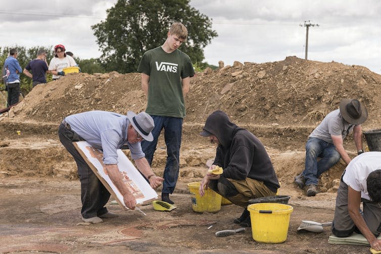 Archaeology students observe Dr. David Neal, expert on mosaics, as he draws a scaled plan of the Trojan War mosaic.