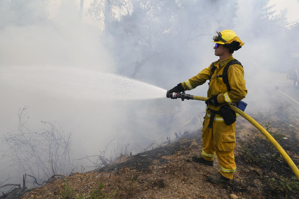 Firefighter Cody Nordstrom, of the North Central Fire station out of Kerman, Calif., hoses down a hot spot along Empire Grade Rd. while fighting the CZU Lightning Complex Fire on Sunday, Aug. 23, 2020, in Bonny Doon, Calif. (AP Photo/Marcio Jose Sanchez)