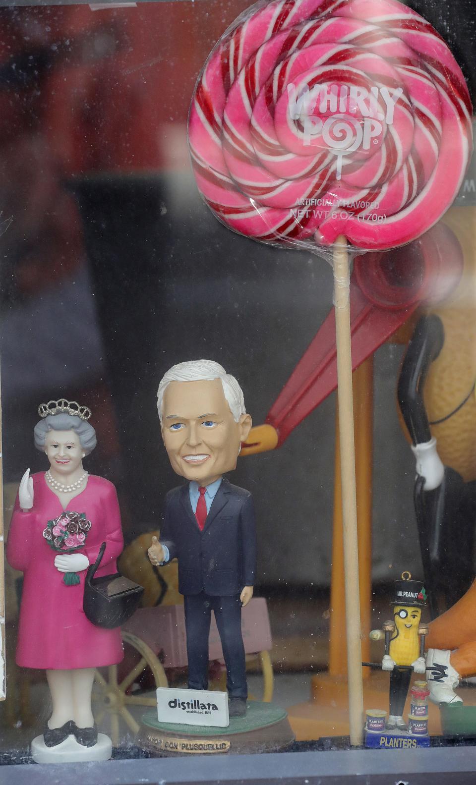 A Queen Elizabeth II figurine and a Mayor Don Plusquellic bobblehead stand in the front window of the Peanut Shoppe in downtown Akron.