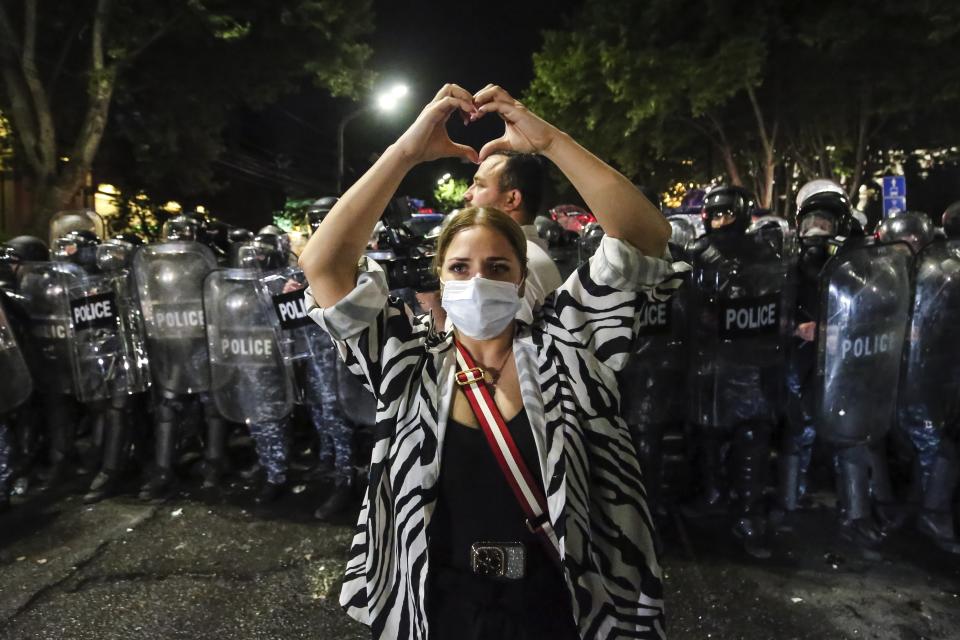 A woman shows a heart standing in front of riot police during an opposition protest against "the Russian law" near the Parliament building in Tbilisi, Georgia, on Wednesday, May 1, 2024. Clashes erupted between police and opposition demonstrators protesting a new bill intended to track foreign influence that the opposition denounced as Russia-inspired. (AP Photo/Zurab Tsertsvadze)