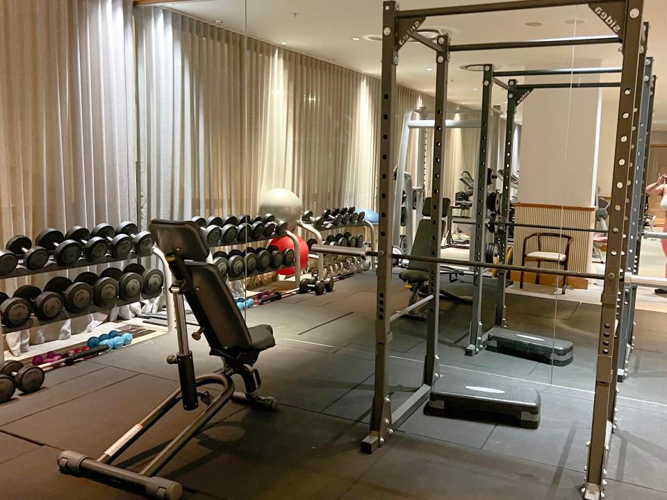 A gym with weights, an upper-body machine, exercise balls, and the reflection of the equipment in a mirror