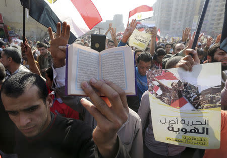 A supporter of the Muslim Brotherhood and ousted Egyptian President Mohamed Mursi holds a copy of the Koran as others shout slogans against the military and the interior ministry during a protest in the Cairo suburb of Matariya November 28, 2014. REUTERS/Mohamed Abd El Ghany