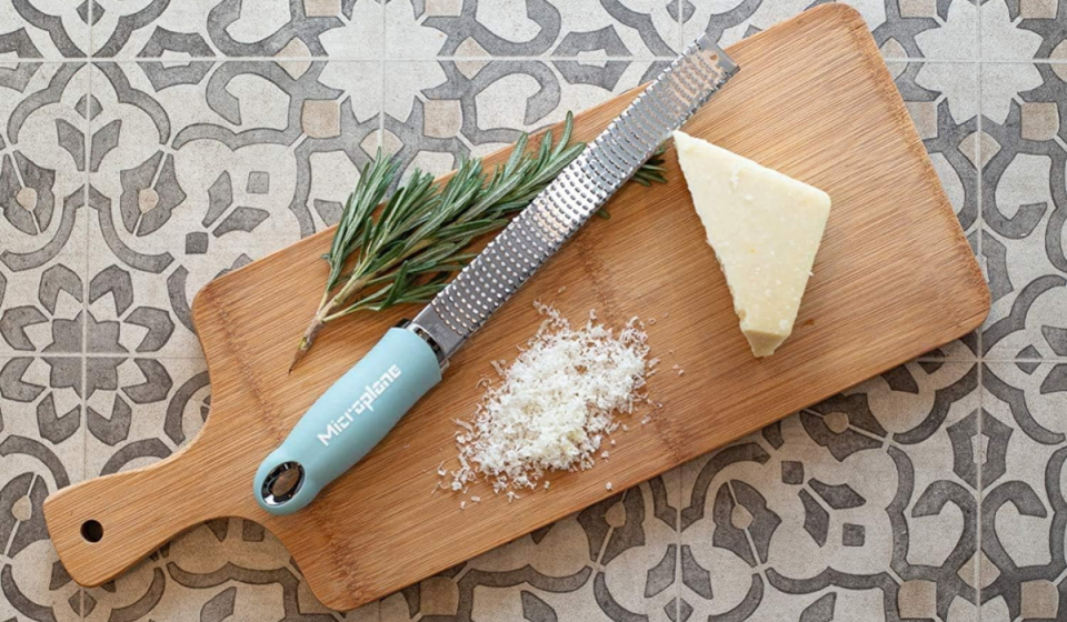 a blue microplane on a cutting board along with grated cheese and rosemary