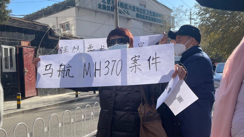 Family members of passengers on board flight MH370 hold up signs demanding an open trail near a court in Beijing's Chaoyang district during a closed-door hearing on November 27, 2023. - CNN