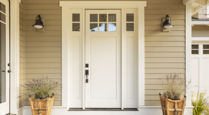 DOOR stock: a white front door of a house between two wall-mounted lights and two potted plants