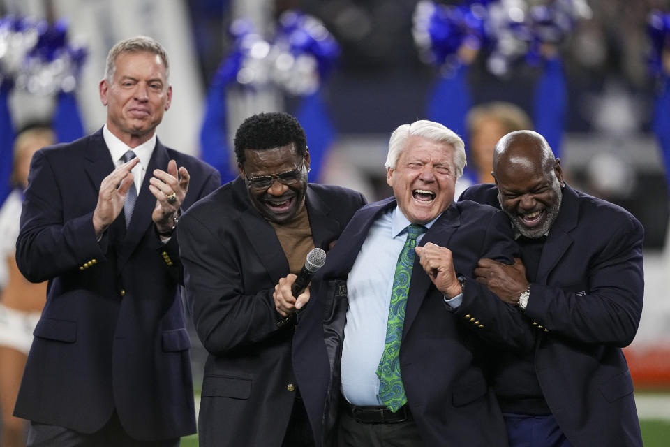 Pro Football Hall of Fame coach Jimmy Johnson, second from right, reacts while speaking next to his former players, from left, Troy Aikman, Michael Irvin and Emmitt Smith during a ceremony inducting Johnson into the team's ring of honor at halftime of an NFL football game between the Cowboys and the Detroit Lions, Saturday, Dec. 30, 2023, in Arlington, Texas. (AP Photo/Sam Hodde)