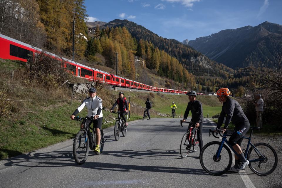 Cyclists watch as a train with 100 cars passes near Bergun, Switzerland, on October 29, 2022, during a record attempt by the Rhaetian Railway (RhB) of the World's longest passenger train, to mark the Swiss railway operator's 175th anniversary.