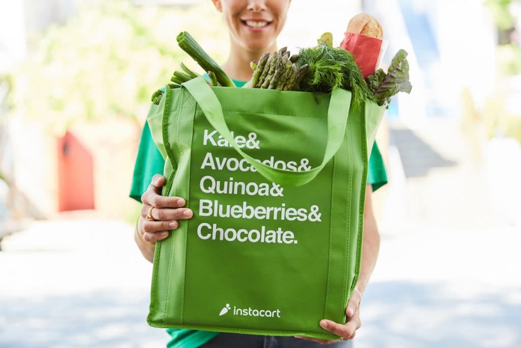 a woman holding an instacart groecery bag full of produde