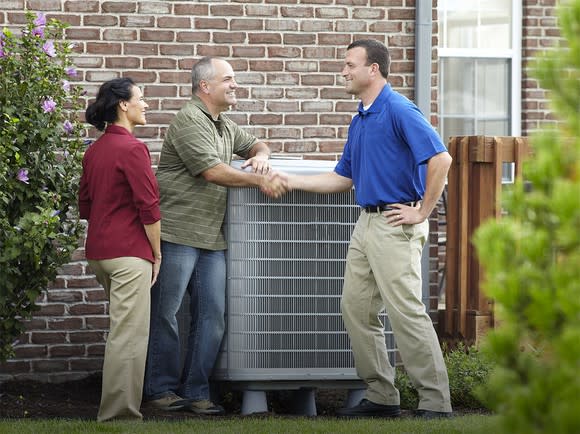 Three people around an air conditioner outside next to a home, with two shaking hands.