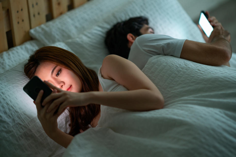 couple in bed looking at their smartphones facing away from each other