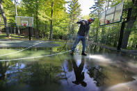 In this Thursday, June 4, 2020 photo, trip leader Gordon Anderson power washes an outdoor basketball court at the Camp Winnebago summer camp in Fayette, Maine. The boys camp is going ahead with plans to open with a reduction in the number of campers and other changes to comply with guidelines for helping prevent the spread of the coronavirus. Many of the nation's 15,000-plus summer camps opting to close because of health concerns surrounding the pandemic, or because of delays in receiving rules or guidelines from licensing officials. (AP Photo/Robert F. Bukaty)