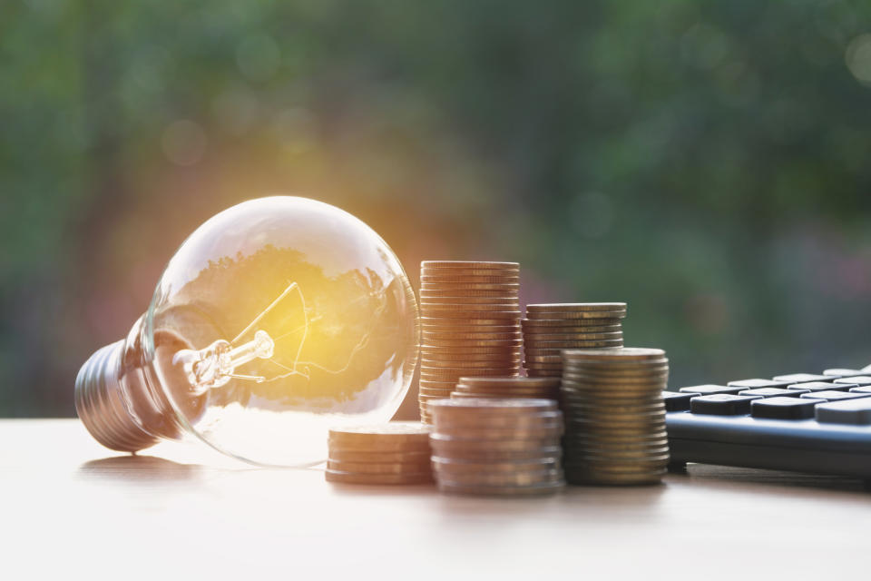 An illuminated light bulb next to stacks of coins and a calculator.