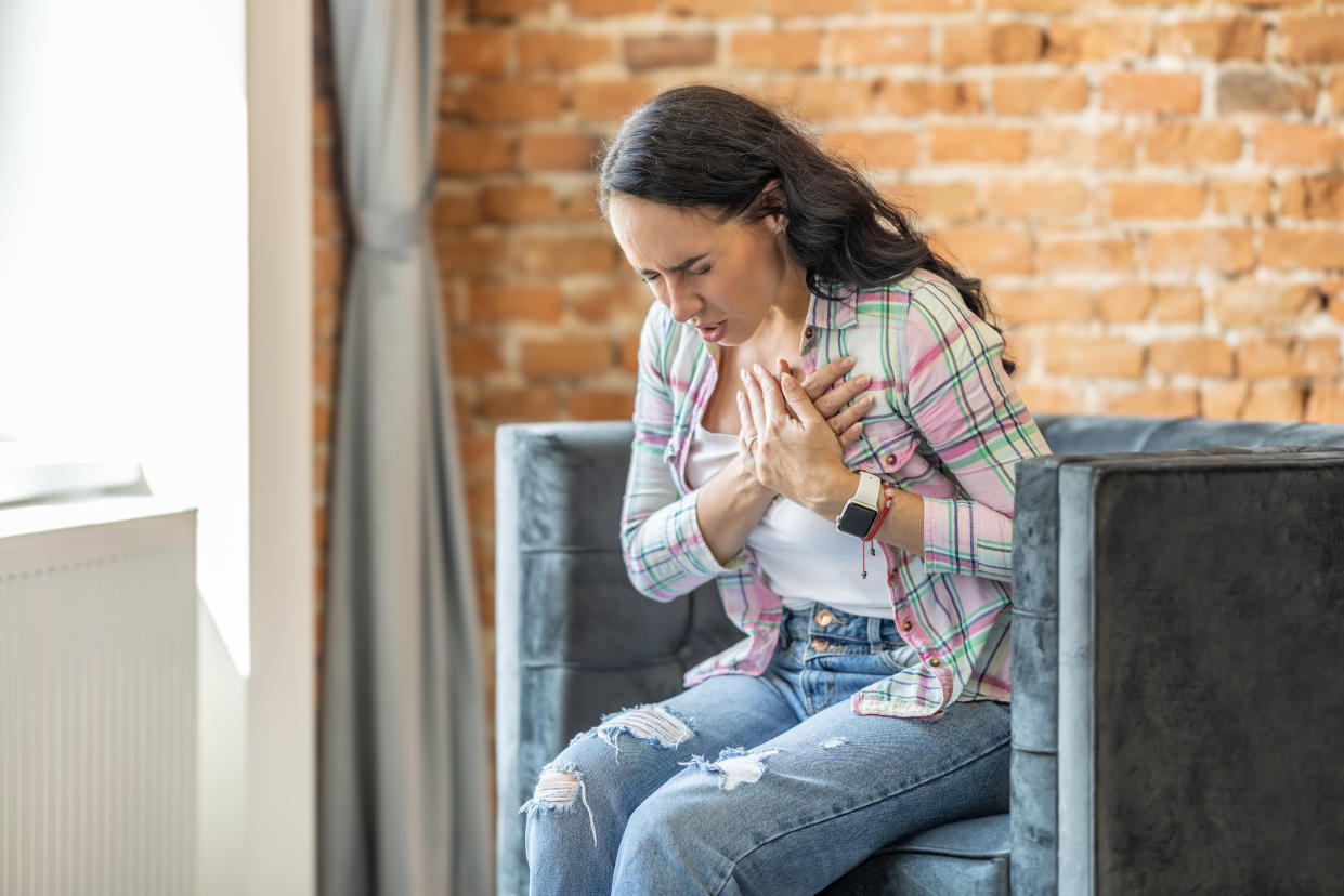 Young woman having heart attack at home. Brunette woman with pain on heart in livingroom.