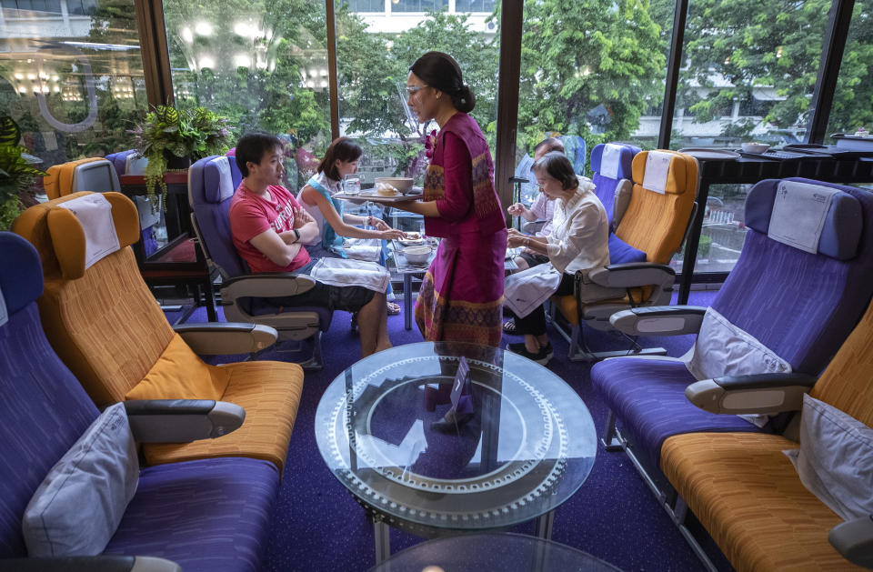 A flight attendant serves meals in a flight-themed restaurant at the Thai Airways head office in Bangkok, Thailand on Oct. 3, 2020. The airline is selling time on its flight simulators to wannabe pilots while its catering division is serving meals in a flight-themed restaurant complete with airline seats and attentive cabin crew. The airline is trying to boost staff morale, polish its image and bring in a few pennies, even as it juggles preparing to resume international flights while devising a business reorganization plan. (AP Photo/Sakchai Lalit)