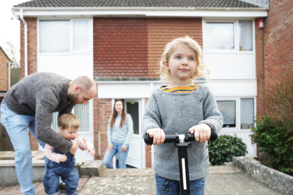 Young girl on pedal scooter with family in front of home