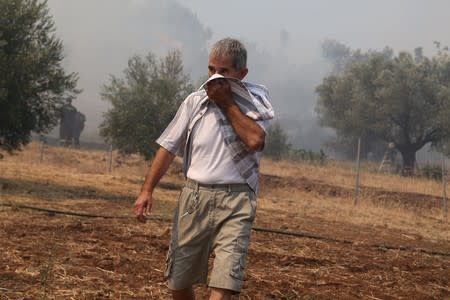 A man covers his face to avoid inhaling smoke as a wildfire burns in the village of Makrimalli on the island of Evia