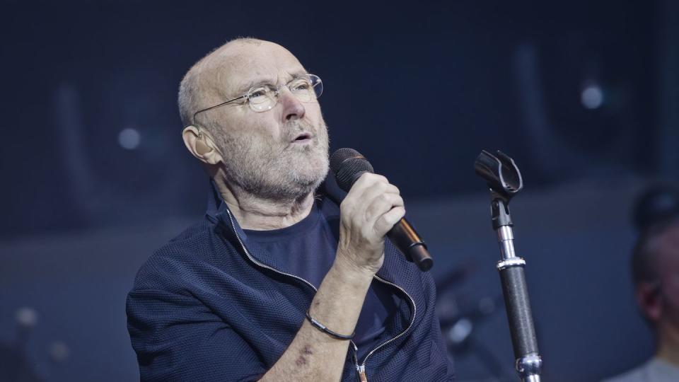 phil collins holding a microphone and singing