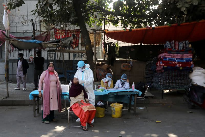 A healthcare worker collects a swab sample from a woman, in New Delhi