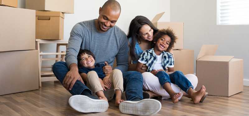 Young couple sits on floor with two children surrounded by moving boxes.