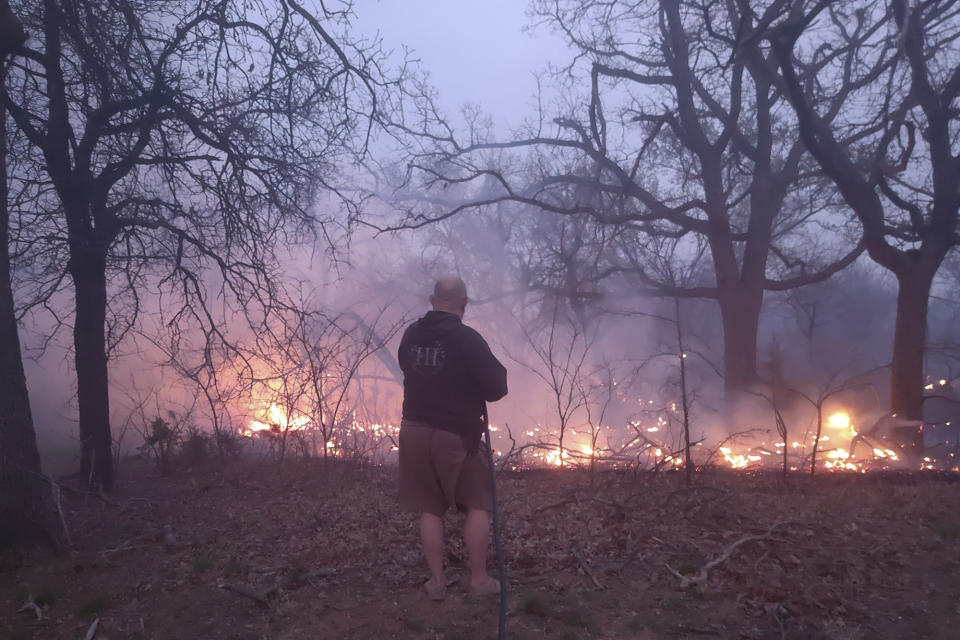 In this photo provided by Jessica Garinger, her father, Jim Garinger, fights a fire outside his home built by his great-grandfather, Friday, March 31, 2023, in Guthrie, Okla. Garinger and his family were able to save his family home with the help of firefighters. Extremely dry conditions in Oklahoma combined with high winds to fuel several large wildfires that forced interstate closures and sent residents fleeing from their homes. (Jessica Garinger via AP)