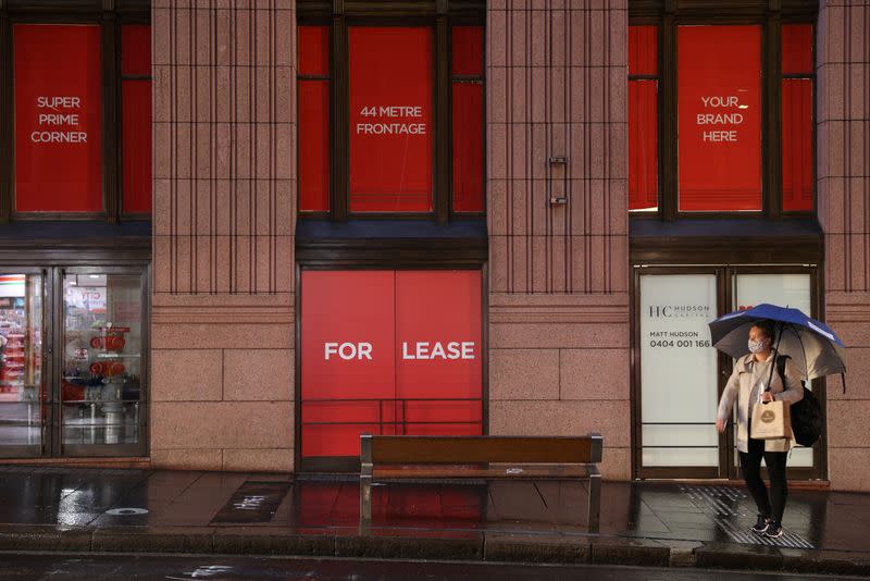 A masked woman waits for a bus in front of real estate up for lease in the heart of the city centre in Sydney