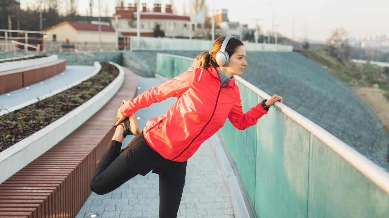  Woman stretching during workout while wearing headphones and sports watch 