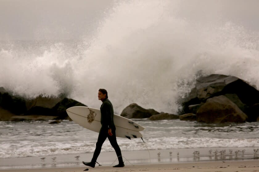 VENICE, CA - JANUARY 15, 2022 - - A surfer walks past the breakwater as tsunami warnings did not keep surfers away from Venice on January 15, 2022. Southland beaches were under a tsunami warning after an underwater volcano erupted in the South Pacific. People were advised to move off the beach and out of the harbors and marinas, avoid the coastline and not to go to the coast to watch the tsunami. (Genaro Molina / Los Angeles Times)