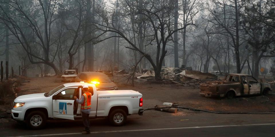 A PG&E vehicle and worker in the foreground of a charred forest scene after the devastating Camp Fire of 2018.