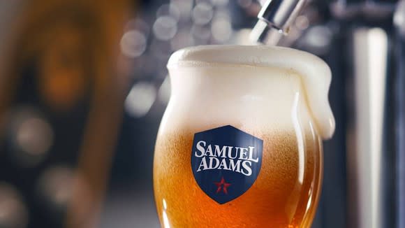 A Samuel Adams beer glass at a tap with foam spilling over