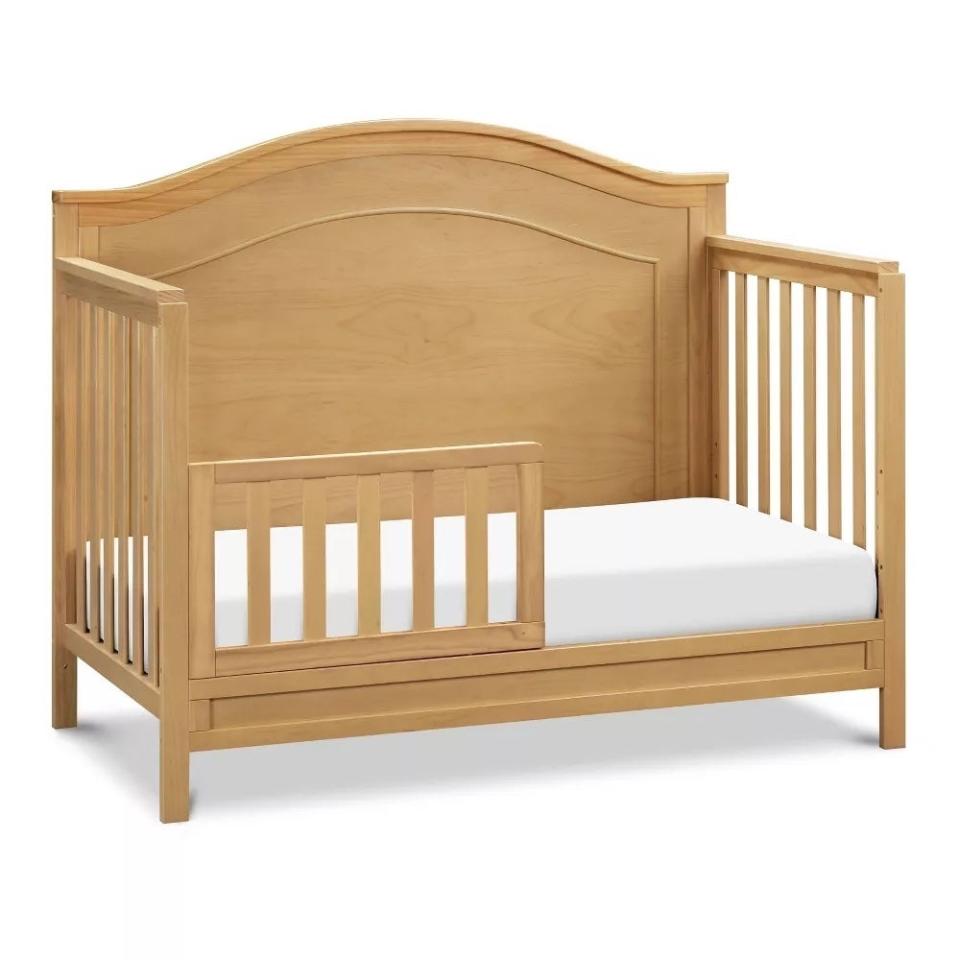 Wooden toddler bed with safety rail and arched headboard design. Suitable for a child's bedroom