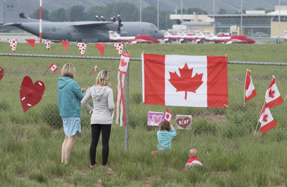 The Canadian Forces Snowbirds jets are seen in the background as a family pays their respects in Kamloops, B.C., Monday, May 18, 2020. Capt. Jenn Casey died Sunday after the Snowbirds jet she was in crashed shortly after takeoff. The pilot of the aircraft is in hospital with serious injuries. (Jonathan Hayward/The Canadian Press via AP)