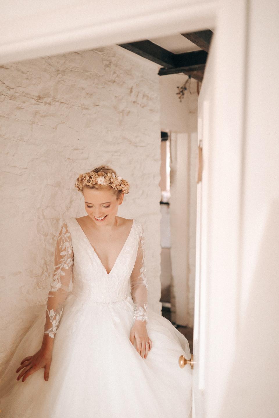 A person poses in a wedding dress in a hallway with white walls.