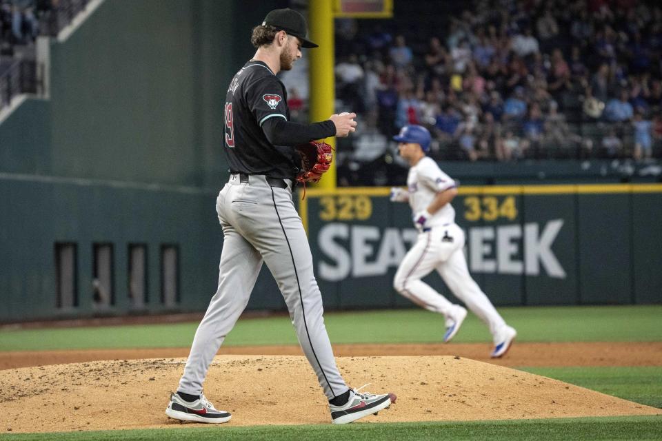 Arizona Diamondbacks starting pitcher Ryne Nelson walks back to the mound after giving up a two run home run to Texas Rangers' Corey Seager, background, during the fifth inning of a baseball game Wednesday, May 29, 2024, in Arlington, Texas. (AP Photo/Jeffrey McWhorter)
