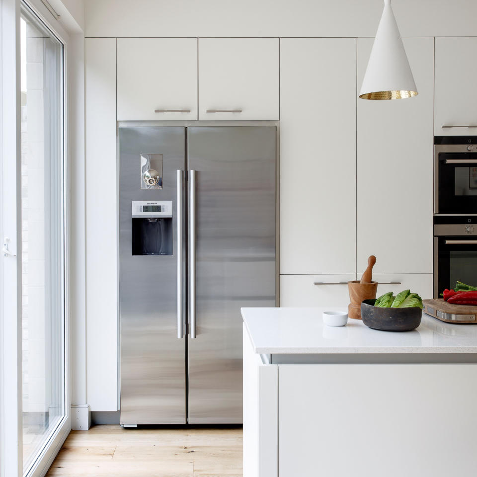 Kitchen with white cabinets, wall, lamps, and kitchen peninsula, wooden floor, metal fridge, and colourful decorative touches