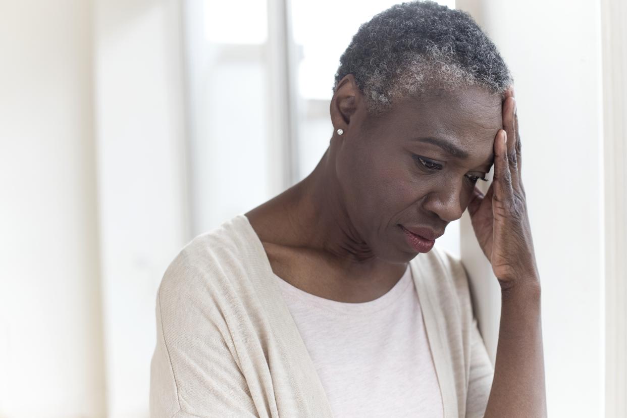 Mature woman touching forehead with pensive expression.