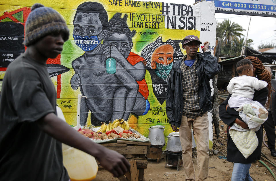 FILE - In this July 8, 2020, file photo, people walk past an informational mural warning people about the dangers of the new coronavirus and how to prevent transmission, with words in Swahili reading "We are the Cure", painted by youth artists from the Uweza Foundation, in the Kibera slum, or informal settlement, of Nairobi, Kenya. A dangerous stigma has sprung up around the coronavirus in Africa — fueled, in part, by severe quarantine rules in some countries as well as insufficient information about the virus. (AP Photo/Brian Inganga, File)