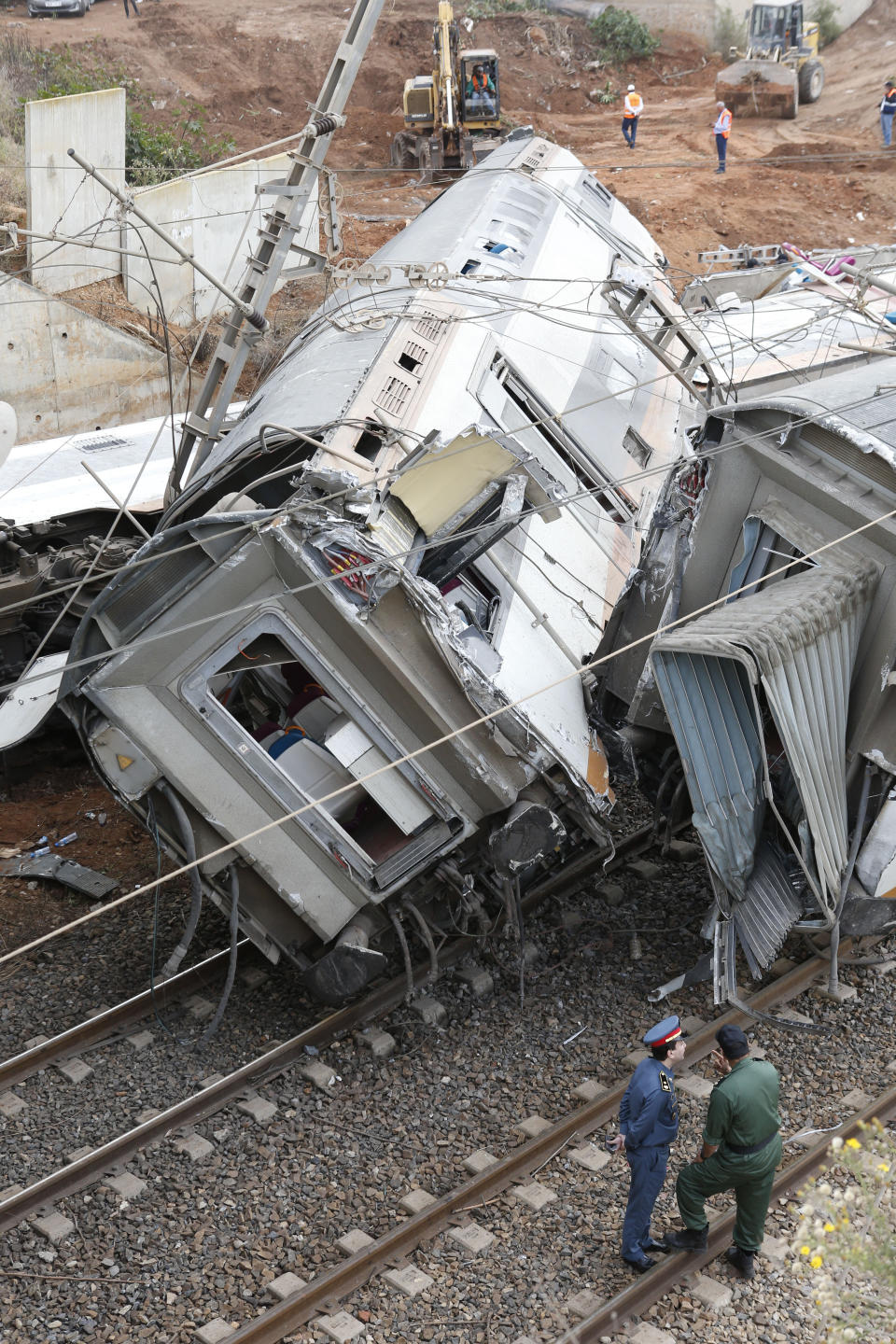 Train employees stand by a derailed train Tuesday Oct.16, 2018 near Sidi Bouknadel, Morocco. A shuttle train linking the Moroccan capital Rabat to a town further north on the Atlantic coast derailed Tuesday, killing several people and injuring dozens, Moroccan authorities and the state news agency said. (AP Photo/Abdeljalil Bounhar)