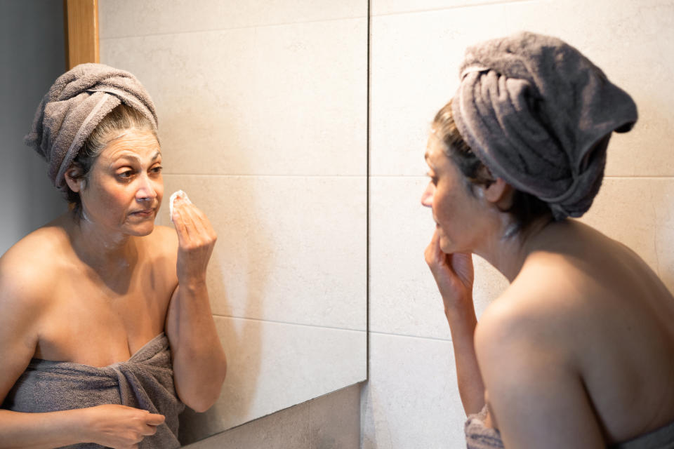 woman wiping off the remains of moisturizer and face mask after a treatment in the bathroom of her home in front of the mirror