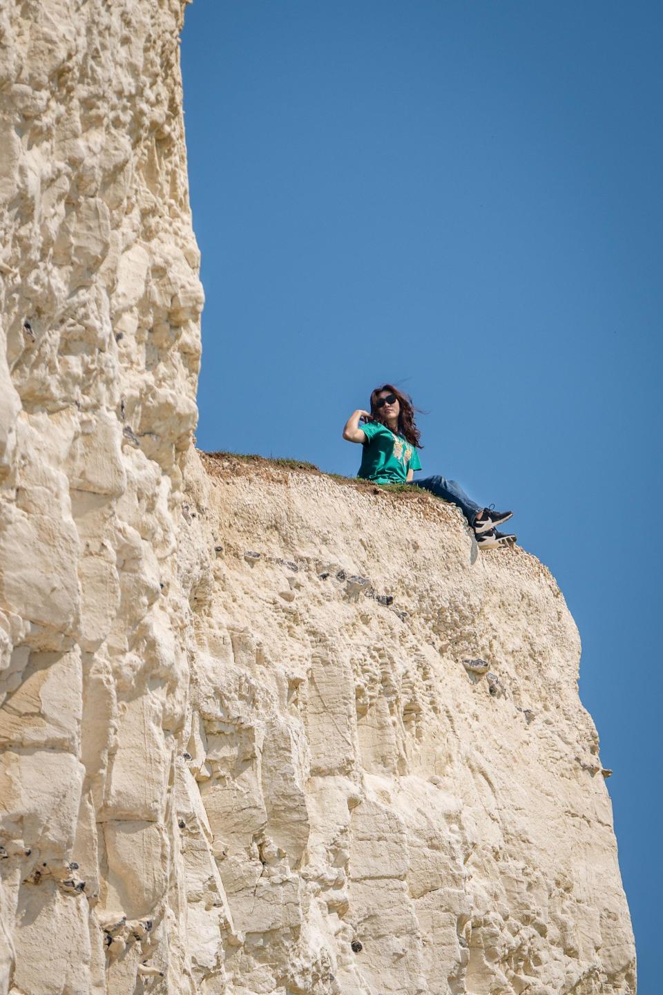 Beachy Head, East Sussex, UK. 11 May, 2024. A tourist poses for photos with their legs over the crumbling cliff edge 4oo feet up on the coast near Birling Gap as temperature are predicted to hit 27C today on hottest weekend of the year so far. Beachy Head, East Sussex, UK Credit: reppans/Alamy Live News