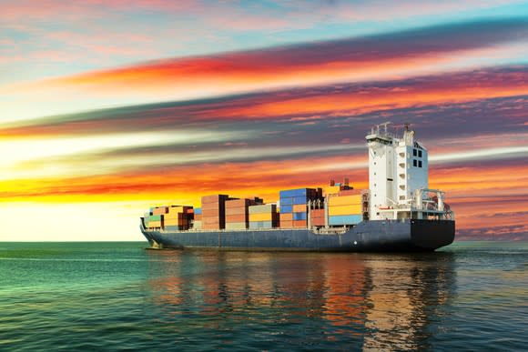 A sailing container ship at sunset on the sea.