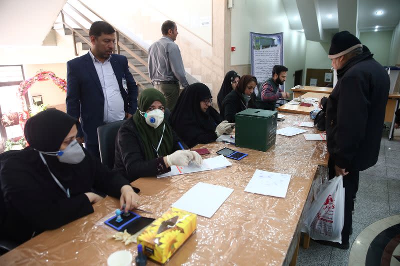 Poll workers wear face masks during parliamentary elections at a polling station in Tehran