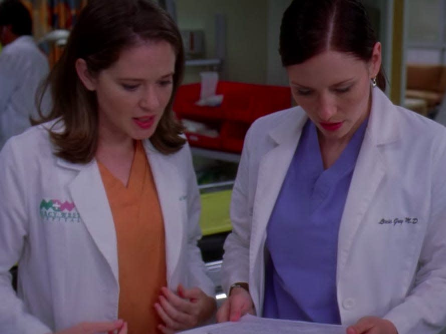 April and Lexie in scrubs and white coats looking over a document together on greys anatomy