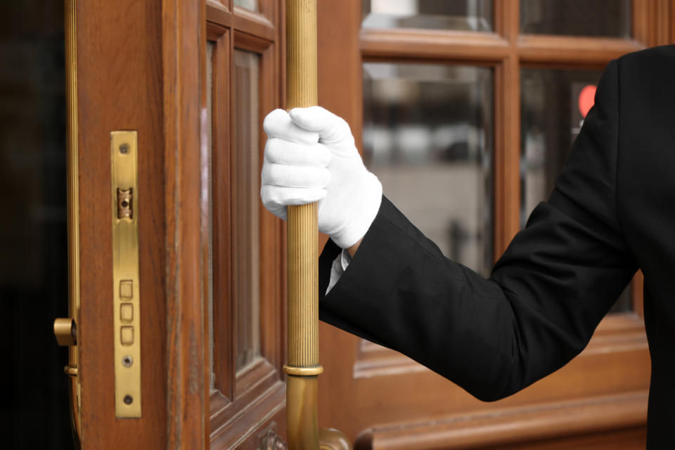 A doorman in a suit and white gloves is holding open a wooden door