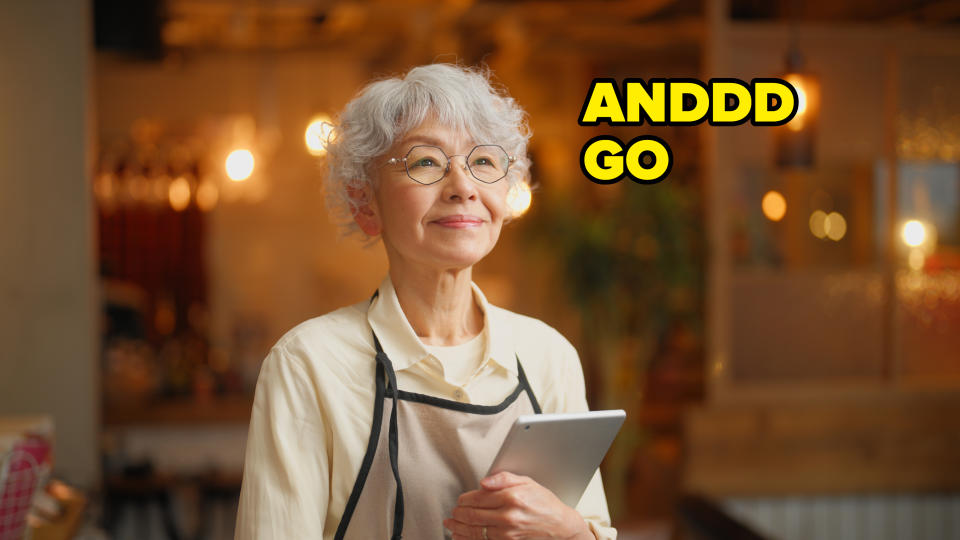 Older woman with glasses holding a tablet, wearing an apron, with a reflective, content expression
