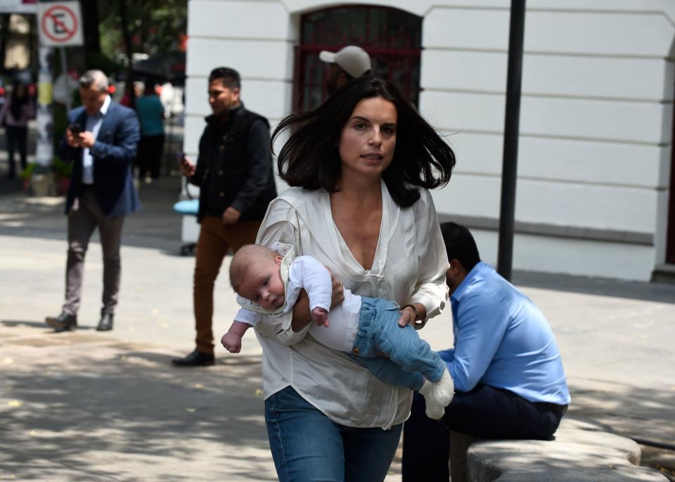 A woman carrying her baby rushes through&nbsp;the street.