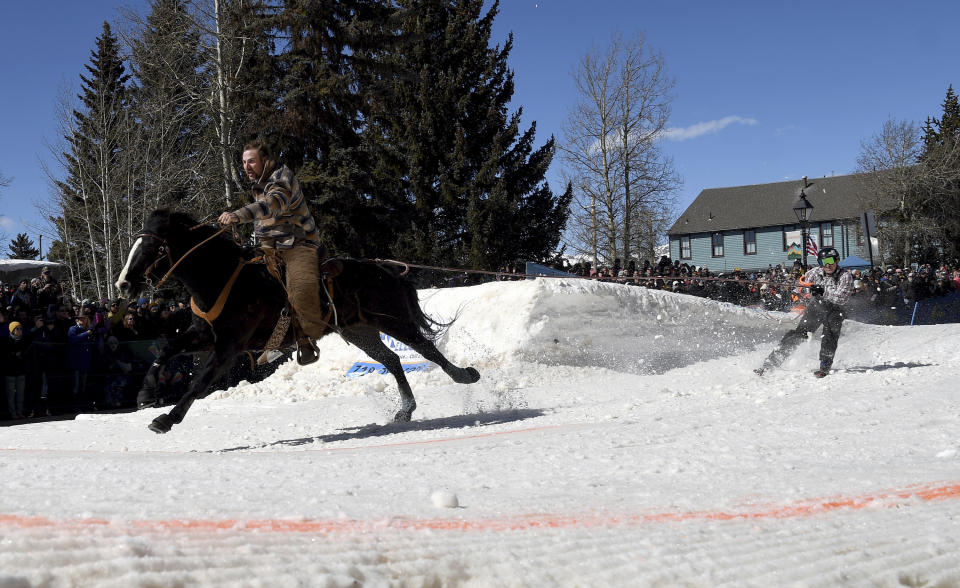 A skijoring team competes in Leadville, Colo., on Saturday, March 2, 2024. Skijoring draws its name from the Norwegian word skikjoring, meaning "ski driving." It started as a practical mode of transportation in Scandinavia and became popular in the Alps around 1900. Today's sport features horses at full gallop towing skiers by rope over jumps and around obstacles as they try to lance suspended hoops with a baton, typically a ski pole that's cut in half. (AP Photo/Thomas Peipert)